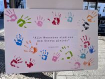Leinwand mit dem Artikel 2 des Grundgesetzes: Alle Menschen sind vor dem Gesetz gleich. Hierauf sind farbige Handabdrücke gedruckt