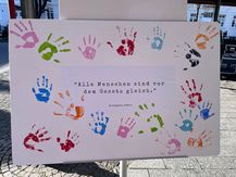 Leinwand mit dem Artikel 2 des Grundgesetzes: Alle Menschen sind vor dem Gesetz gleich. Hierauf sind farbige Handabdrücke gedruckt