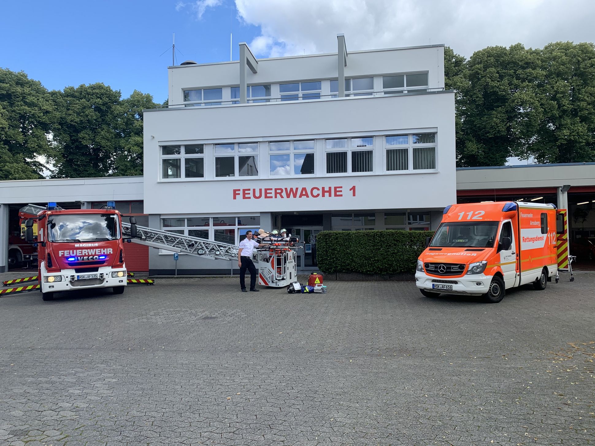 Rettungsdienstmitarbeiter zwischen einer Drehleiter und einem RTW mit Übungsmaterial